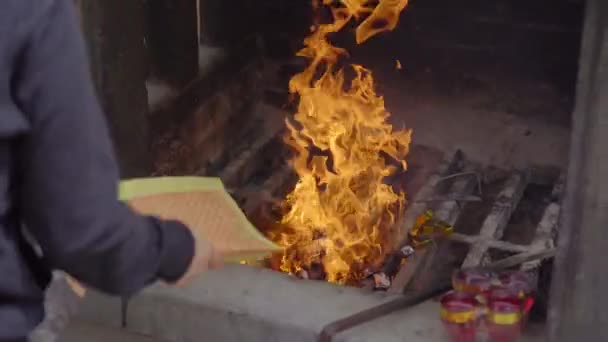 Člověk pálí joss papíry nebo obětní papíry v buddhistickém chrámu — Stock video