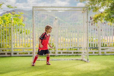 Kırmızı futbol forması giyen, futbol oynayan, sahada, dışarıda futbol oynayan tatlı bir çocuk. Aktif çocuk çocuklarla ya da babayla spor yapıyor, gülen mutlu çocuk yazın eğleniyor.