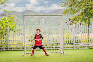 Kırmızı futbol forması giyen, futbol oynayan, sahada, dışarıda futbol oynayan tatlı bir çocuk. Aktif çocuk çocuklarla ya da babayla spor yapıyor, gülen mutlu çocuk yazın eğleniyor.