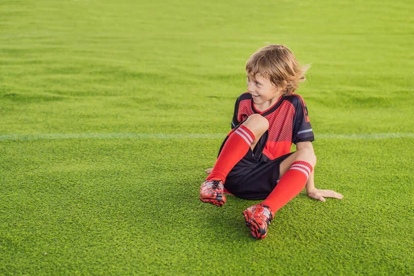 Kleiner süßer Junge in roter Fußballuniform, der Fußball spielt, Fußball auf dem Feld, im Freien. Aktives Kind, das mit Kindern oder Vater Sport treibt, lächelnder fröhlicher Junge, der Spaß im Sommer hat — Stockfoto