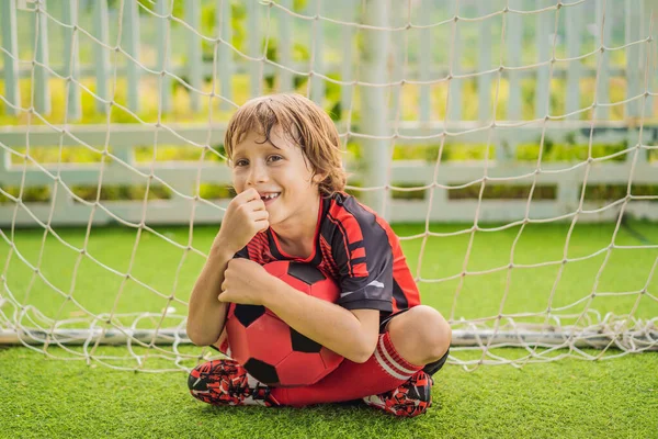 Little cute kid boy in red football uniform playing soccer, football on field, outdoors. Active child making sports with kids or father, Smiling happy boy having fun in summer — Stock Photo, Image