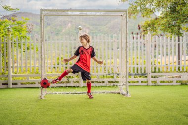 Kırmızı futbol forması giyen, futbol oynayan, sahada, dışarıda futbol oynayan tatlı bir çocuk. Aktif çocuk çocuklarla ya da babayla spor yapıyor, gülen mutlu çocuk yazın eğleniyor.