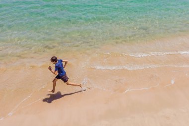 Sahilde koşan bir koşucu okyanus manzaralı. Erkek sporcu sabah antrenmanı yaparak kardiyo antrenmanı yapıyor. Kahraman hava aracı görüntüsü, bir sürü kopya alanı