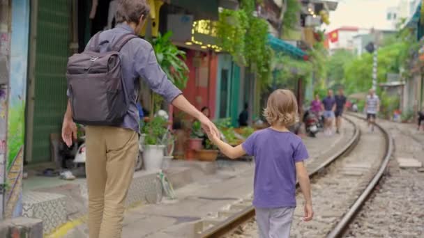 Młody ojciec i jego syn podróżnicy zwiedzać obszar miasta Hanoi, gdzie ścieżki kolejowe przejść przez dzielnicy mieszkalnej. Hanoi Train Street jest znanym miejscem turystycznym — Wideo stockowe
