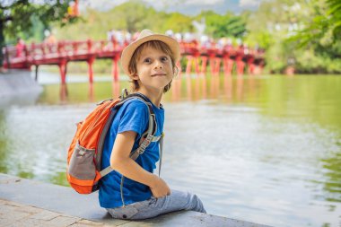 Hanoi şehir merkezindeki Hoan Kiem Gölü 'nün ortasında ağaçlarla çevrili Kızıl Köprü' nün arka planındaki beyaz çocuk turist. Çocuk konseptiyle seyahat etmek
