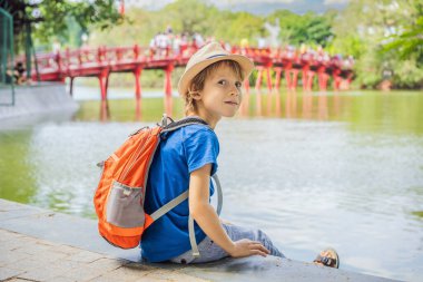 Hanoi şehir merkezindeki Hoan Kiem Gölü 'nün ortasında ağaçlarla çevrili Kızıl Köprü' nün arka planındaki beyaz çocuk turist. Çocuk konseptiyle seyahat etmek