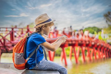 Hanoi şehir merkezindeki Hoan Kiem Gölü 'nün ortasında ağaçlarla çevrili Kızıl Köprü' nün arka planındaki beyaz çocuk turist. Çocuk konseptiyle seyahat etmek