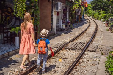 Mother and son travelers walk around railway paths which go through residential area in Hanoi city. Hanoi Train Street is a famous tourist destination. Vietnam reopens after coronavirus quarantine clipart