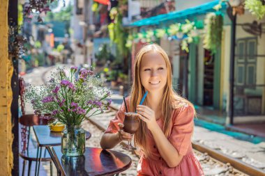 Genç bayan gezgin kahve içiyor Hanoi şehrinin yerleşim alanından geçen tren yolunun kenarında oturuyor. Hanoi Tren Sokağı ünlü bir turizm merkezidir. Vietnam Coronavirüs 'ten sonra yeniden açılıyor.