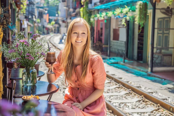 Genç bayan gezgin kahve içiyor Hanoi şehrinin yerleşim alanından geçen tren yolunun kenarında oturuyor. Hanoi Tren Sokağı ünlü bir turizm merkezidir. Vietnam Coronavirüs 'ten sonra yeniden açılıyor.
