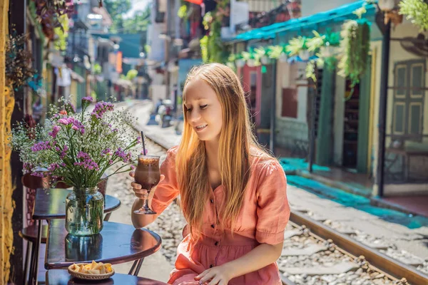 Молодая женщина-путешественница пьет кофе сидя на железнодорожных путях, которые проходят через жилой район в городе Ханой. Ханой Трейн-стрит является известным туристическим направлением. Вьетнам открывается после коронавируса — стоковое фото