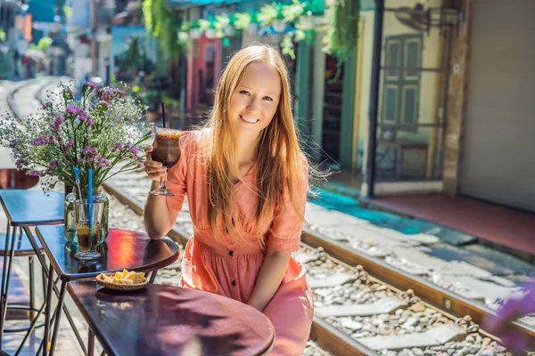Genç bayan gezgin kahve içiyor Hanoi şehrinin yerleşim alanından geçen tren yolunun kenarında oturuyor. Hanoi Tren Sokağı ünlü bir turizm merkezidir. Vietnam Coronavirüs 'ten sonra yeniden açılıyor.