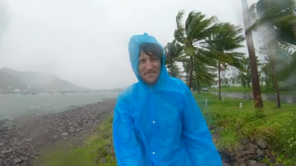 Slowmotion video. A man in a raincoat is under a hevy rain and stormy wind. Shot on an action camera. Tropical storm . Contains natural sound — ストック動画