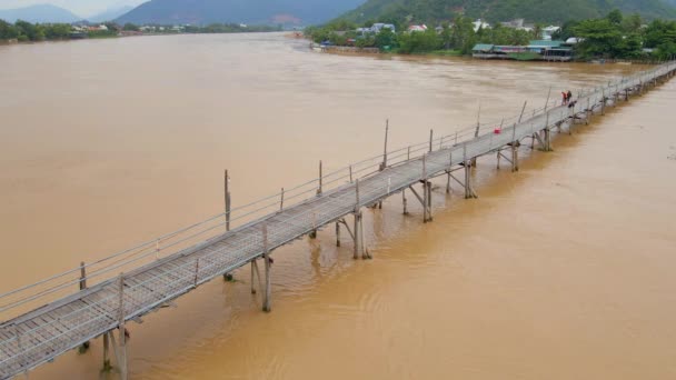 アジアの川を渡る木製の橋の空中スローモーションショットで、バイクが乗っています。危険物輸送の概念 — ストック動画
