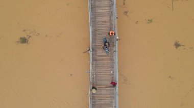 Asya 'da nehir boyunca üzerinde motosikletler olan ahşap bir köprünün havadaki yavaş çekimi. Tehlikeli ulaşım yapıları kavramı