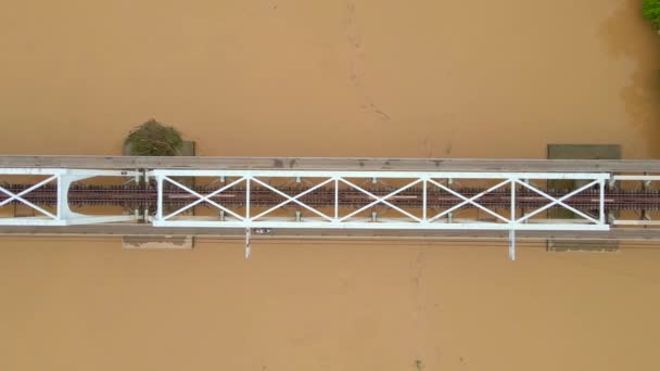 Luchtfoto slow motion van een metalen spoorbrug over een rivier, die een bruin-gele kleur heeft — Stockvideo