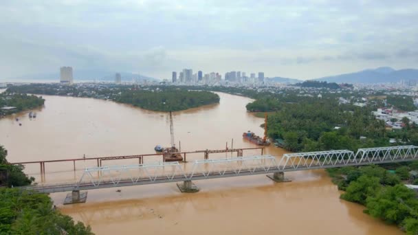 Fotografia em câmara lenta aérea de uma ponte ferroviária metálica sobre um rio, que tem uma cor amarelo-acastanhada. Atrás da ponte está outro a ser construído. — Vídeo de Stock