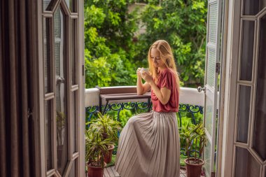 Kızıl saçlı bir kadın miras tarzı bir balkonda sabah kahvesinin tadını çıkarıyor. Avrupa 'da ya da Asya' da bir otelde kalan bir kadın, bir salgından sonra iyileşiyor. Turizm sayesinde düzeldi.