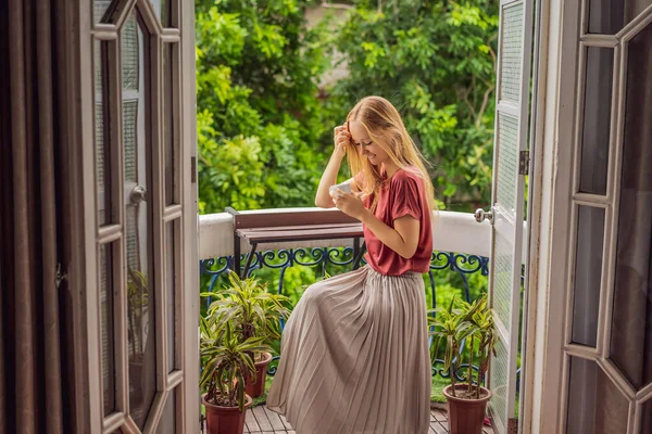 Uma mulher ruiva fica em uma varanda de estilo patrimonial desfrutando de seu café da manhã. Uma mulher em um hotel na Europa ou na Ásia como turismo se recupera de uma pandemia. Turismo recuperou graças a — Fotografia de Stock