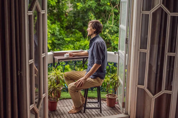 Az ember egy örökség stílusú erkélyen áll, és a reggeli kávéját élvezi. Egy férfi egy európai vagy ázsiai hotelben, ahogy a turizmus felépül egy világjárványból. Az idegenforgalom helyreállt az oltásoknak köszönhetően. Nő — Stock Fotó