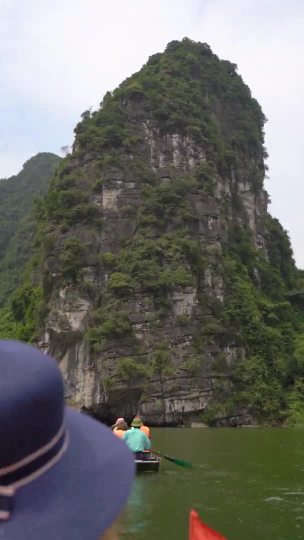 Verticale video. Een jonge vrouw op een boot met een riviertocht tussen spectaculaire kalkstenen rotsen in Ninh Binh, een toeristische bestemming in het noorden van Vietnam. Reis naar Vietnam concept — Stockvideo
