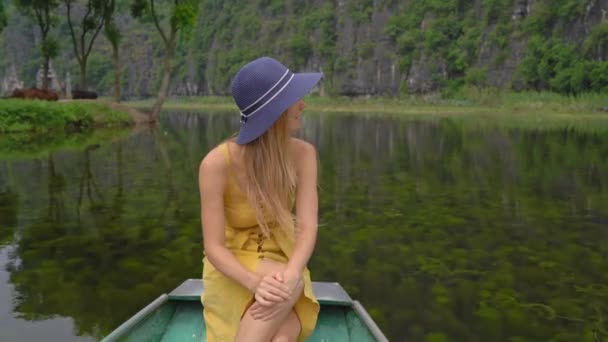 Una mujer joven en un barco que tiene un viaje por el río entre rocas en Ninh Binh, un destino turístico en el norte de Vietnam. Viajar a Vietnam concepto — Vídeos de Stock