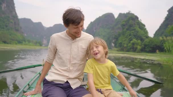 在越南北部的一个旅游胜地宁滨，一个年轻人和他的儿子坐在一条船上，在壮观的石灰岩中游览河流。前往越南的旅行概念 — 图库视频影像