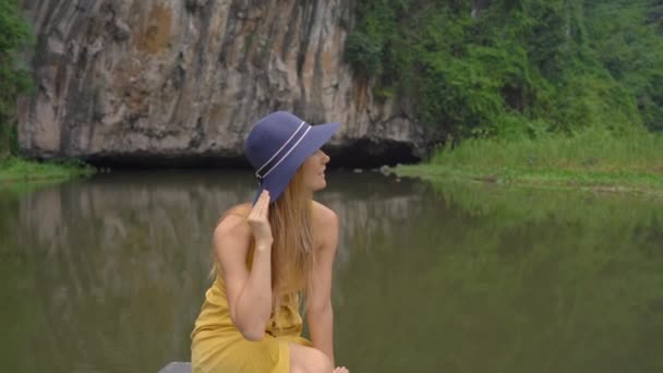 Uma jovem mulher em um barco que tem uma viagem de rio entre rochas em Ninh Binh, um destino turístico no norte do Vietnã. Viajar para Vietnã conceito — Vídeo de Stock