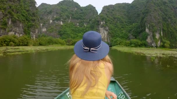 Una joven en un barco que tiene un viaje por el río entre espectaculares rocas de piedra caliza en Ninh Binh, un destino turístico en el norte de Vietnam. Viajar a Vietnam concepto — Vídeo de stock