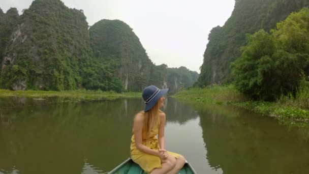 在越南北部的一个旅游胜地宁滨，一名年轻女子坐在一条船上，在壮观的石灰岩中沿河漂流。前往越南的旅行概念 — 图库视频影像