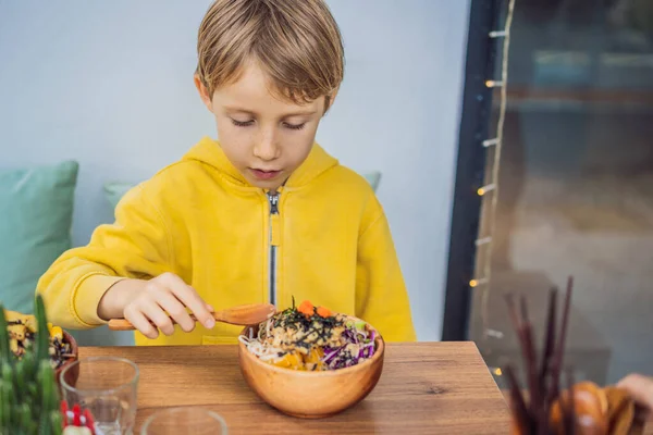 Boy äta rå ekologisk Poke skål med ris och grönsaker närbild på bordet. Ovanifrån horisontellt — Stockfoto