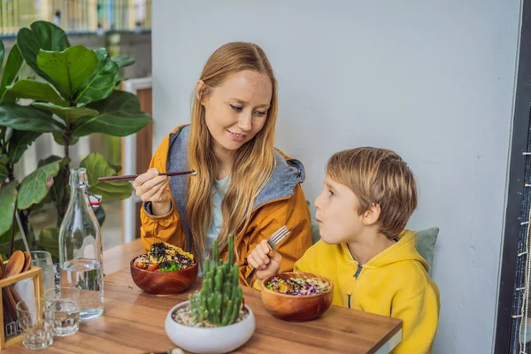 Mor och son äter rå ekologisk Poke skål med ris och grönsaker närbild på bordet. Ovanifrån horisontellt — Stockfoto