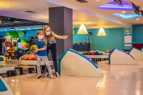 Schöne junge Mutter und Sohn spielen Bowling mit medizinischen Masken während COVID-19 Coronavirus in Bowlingclub — Stockfoto