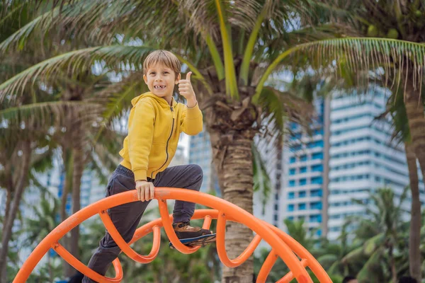 男孩在棕榈树的背景下爬到操场上 — 图库照片