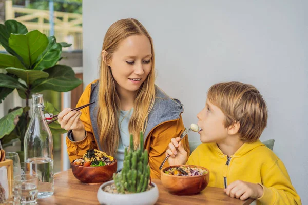 Mor och son äter rå ekologisk Poke skål med ris och grönsaker närbild på bordet. Ovanifrån horisontellt — Stockfoto