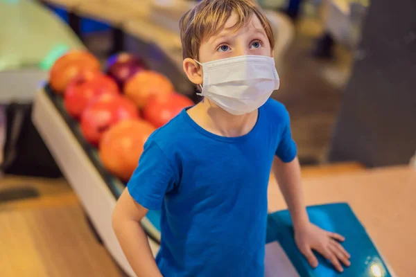 Ragazzo che gioca a bowling con maschere mediche durante COVID-19 coronavirus nel bowling club — Foto Stock