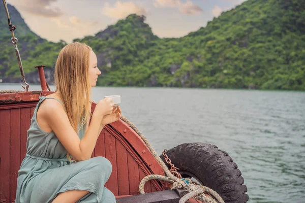 Attractive woman in a dress is drinking coffee, traveling by boat in Halong Bay. Vietnam. Travel to Asia, happiness emotion, summer holiday concept. Picturesque sea landscape. Ha Long Bay, Vietnam — Φωτογραφία Αρχείου