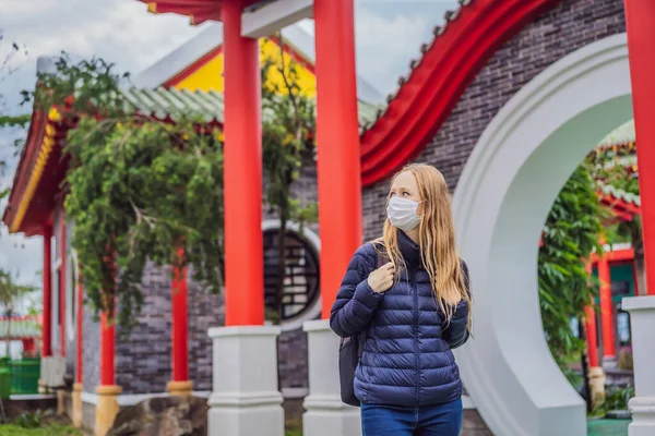 Traveler in medical mask stopped on the street and looking at the Japanese, Chinese, Korean, Vietnamese traditional building. Tourists travel in Asia after the coronavirus epidemic — Stock Photo, Image