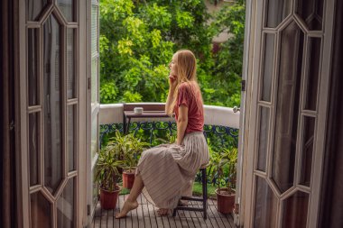 Kızıl saçlı bir kadın miras tarzı bir balkonda sabah kahvesinin tadını çıkarıyor. Avrupa 'da ya da Asya' da bir otelde kalan bir kadın, bir salgından sonra iyileşiyor. Turizm sayesinde düzeldi.