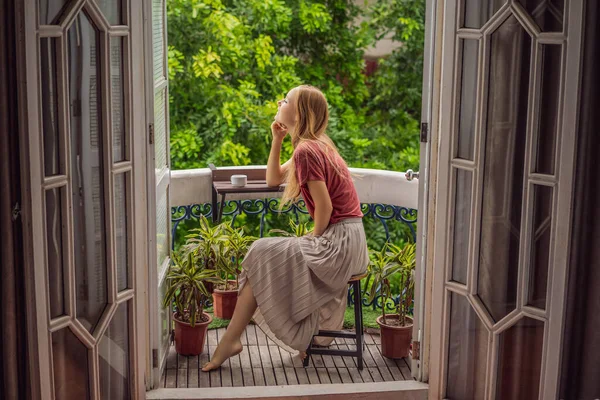 Una donna dai capelli rossi si trova su un balcone in stile heritage che si gode il suo caffè mattutino. Una donna in un hotel in Europa o in Asia mentre il turismo si riprende da una pandemia. Il turismo si è ripreso grazie a — Foto Stock