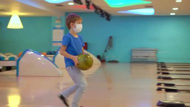 Genç bir kadın ve maske takan küçük oğlu bowling oynuyorlar. Açık alanları ziyaret ederken maske takın