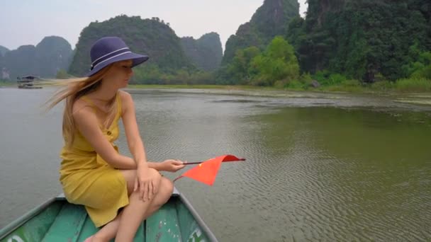 Slowmotion skott av en ung kvinna som håller en vietnamesisk flagga i handen har en flod resa bland spektakulära kalksten stenar i Ninh Binh, ett turistmål i norra Vietnam. Resor till Vietnam — Stockvideo