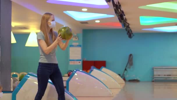 En ung kvinna och hennes son i ansiktsmasker spelar bowling. Bär masker när du besöker offentliga platser — Stockvideo