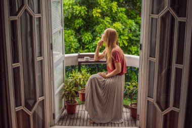 Kızıl saçlı bir kadın miras tarzı bir balkonda sabah kahvesinin tadını çıkarıyor. Avrupa 'da ya da Asya' da bir otelde kalan bir kadın, bir salgından sonra iyileşiyor. Turizm sayesinde düzeldi.