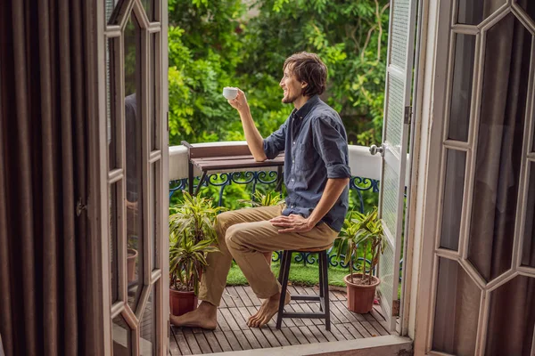 Чоловік стоїть на балконі в стилі спадщини, насолоджуючись його ранковою кавою. Людина в готелі в Європі або Азії, як туризм відновлюється після пандемії. Туризм відновився завдяки вакцинації. Жінка — стокове фото