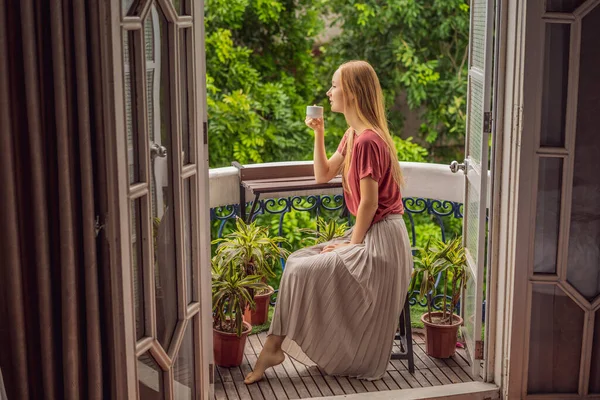 Рукавичка жінка стоїть на балконі в стилі спадщини, насолоджуючись її ранковою кавою. Жінка в готелі в Європі чи Азії, коли туризм відновлюється після пандемії. Туризм відновився завдяки — стокове фото