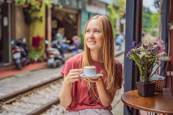 Jeune voyageuse boit du café vietnamien avec œuf assis près des chemins de fer qui traversent le quartier résidentiel de la ville de Hanoi. Hanoi Train Street est une destination touristique célèbre. Le Vietnam rouvre — Photo