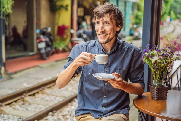 Молодой человек пьет вьетнамский кофе с яйцом сидя на железнодорожных путях, которые проходят через жилой район в городе Ханой. Ханой Трейн-стрит является известным туристическим направлением. Вьетнам вновь открывается — стоковое фото