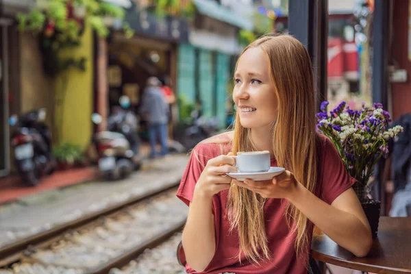 Young woman traveler drinks Vietnamese coffee with egg sitting by the railway paths which go through residential area in Hanoi city. Hanoi Train Street is a famous tourist destination. Vietnam reopens