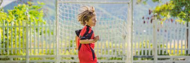 BANNER, BANNER, UZUN kırmızı futbol üniformalı küçük şirin çocuk futbol oynuyor, futbol sahada, dışarıda. Aktif çocuk çocuklarla ya da babayla spor yapıyor, gülen mutlu çocuk yazın eğleniyor.